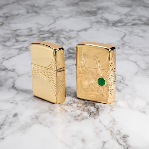 Lifestyle image of Armor Fleur-de-lis Design High Polish Gold Plate Windproof Lighter, showing both sides of lighter, standing on a marble surface